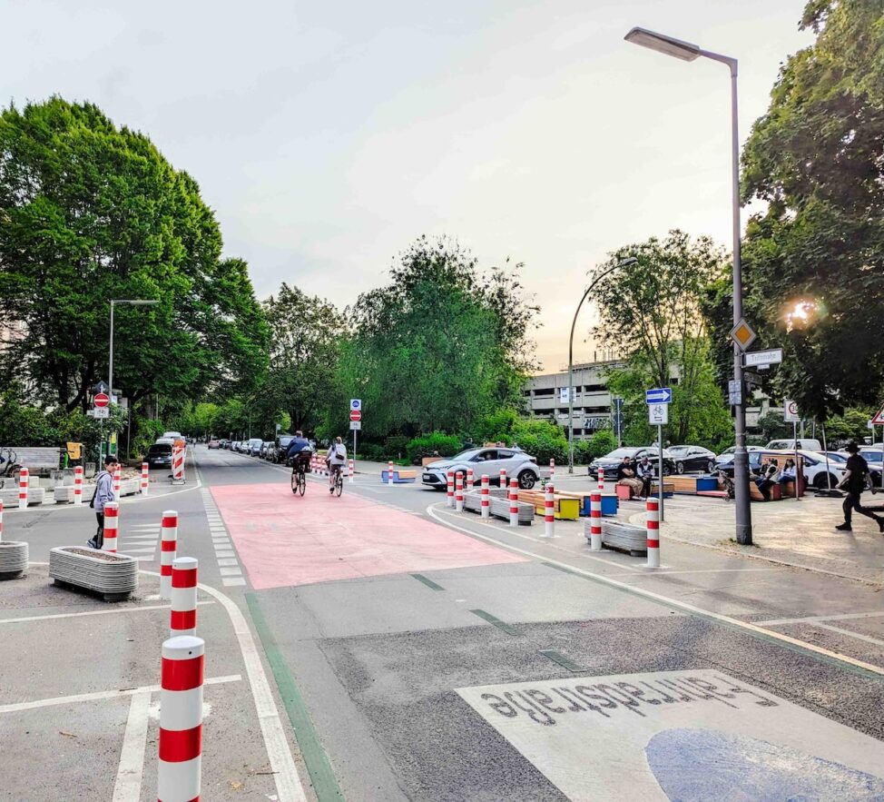 Fahrradstraße mit Fahrzeugen und Radfahrern. Baumkronen im Hintergrund.